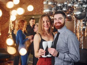 Bearded young man with his girlfriend standing together against their friends in christmas decorated room and celebrating New Year 1